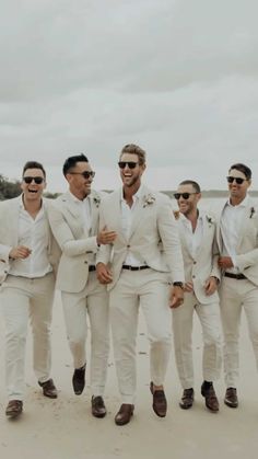 a group of men standing next to each other on top of a sandy beach wearing white suits