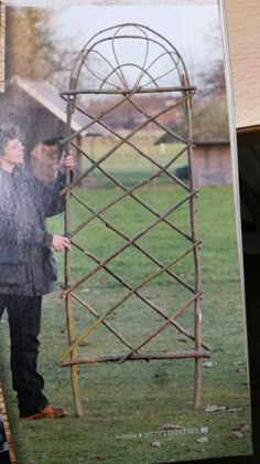 a man holding an umbrella next to a tall wooden trellis on the grass in front of a building