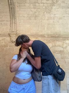 a man and woman kissing each other in front of a brick wall with an arch