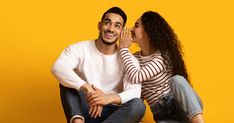 a man and woman sitting next to each other on a yellow background, one is kissing the other's cheek