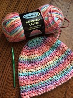 a crocheted hat with yarn next to it on a wooden table and a ball of knitting needles