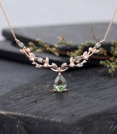 an image of a necklace with leaves and stones on the front, sitting on top of a wooden table