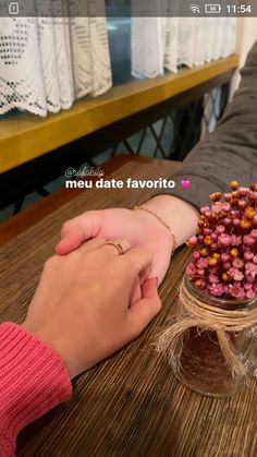 two people holding hands on top of a wooden table next to a vase filled with flowers