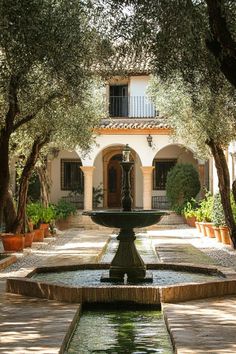 an outdoor fountain in front of a house with potted plants and trees around it