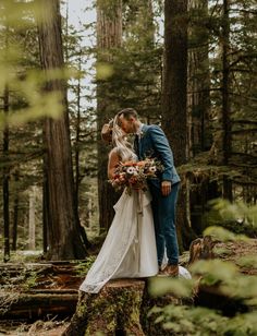 a bride and groom kissing in the woods surrounded by tall trees at their wedding day