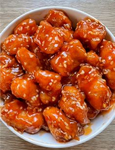 a white bowl filled with meat covered in sesame seeds and teriyaki sauce on top of a wooden table