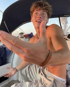 a shirtless man sitting on top of a boat with his hand in the air