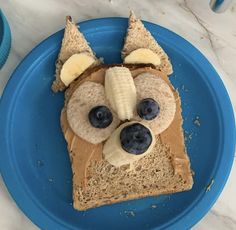 a piece of bread with peanut butter, banana and blueberries in the shape of a dog's face