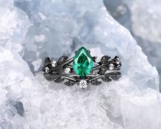 a ring with an emerald colored stone surrounded by white diamonds on top of some ice crystals