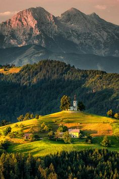 a small church sits on top of a green hill with mountains in the back ground