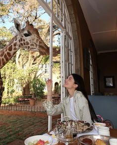 a woman reaching up to feed a giraffe at a table with food on it