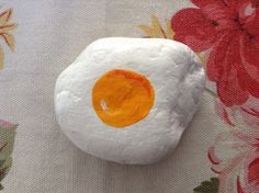 a rock with an egg painted on it sitting on a flowered cloth covered surface