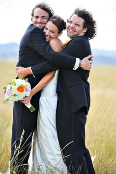 two men and a woman hugging each other in the middle of a field with tall grass