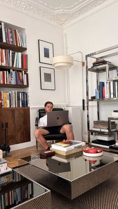 a man sitting on a couch with a laptop in his lap and bookshelves behind him