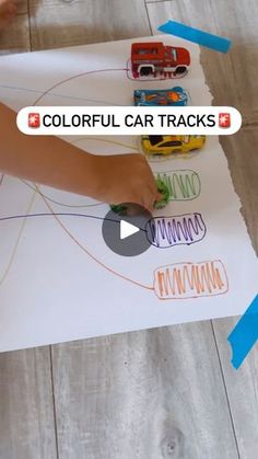 a child's hand writing on a piece of paper with colorful car tracks