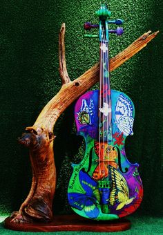 a colorful violin sitting on top of a wooden stand next to a tree branch and green wall