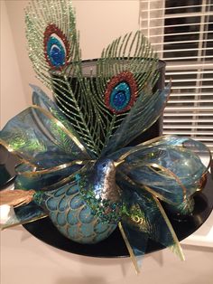 a decorative blue and green hat with peacock feathers on it's head, sitting on a black plate