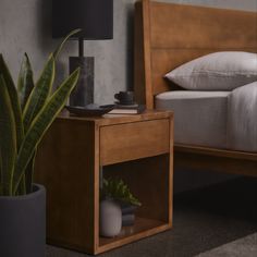 a bed with a wooden headboard next to a night stand and a potted plant