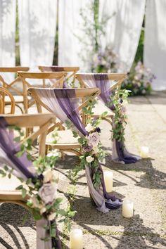 an outdoor ceremony set up with wooden chairs and purple sashes, candles and flowers