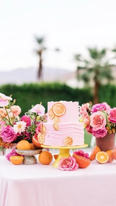 a pink cake sitting on top of a table next to oranges and other fruit