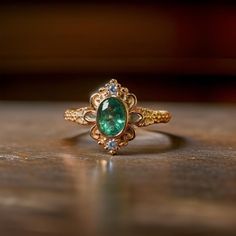 an emerald and diamond ring sitting on top of a wooden table