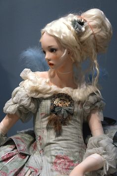 a doll is dressed in a dress with feathers on it's head and hair