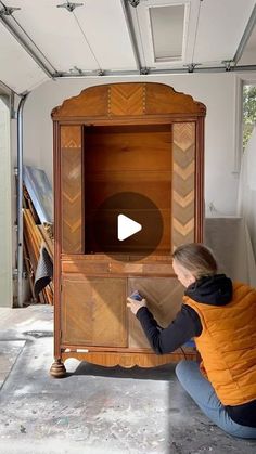 a woman kneeling down next to a wooden cabinet with an arrow on the front and bottom