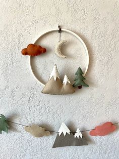 a wall hanging made out of felt with trees and mountains in the background on a string