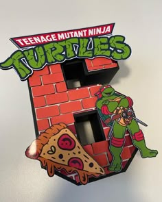 the teenage mutant ninja logo is on top of a red brick wall with a slice of pizza in front of it