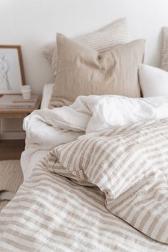 an unmade bed with striped sheets and pillows on top of it, next to a small side table