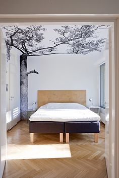 an open door leading to a bedroom with a bed and tree mural on the wall