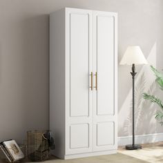 a tall white armoire next to a lamp in a room with a plant on the floor