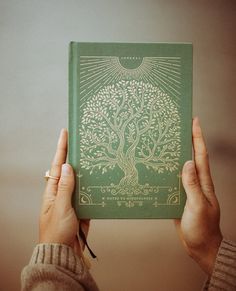 a person holding up a green book with a tree on it