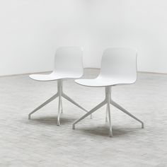 two white chairs sitting next to each other on top of a tile floor in an empty room