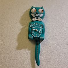 a blue cat clock on the wall with eyes and nose painted on it's face