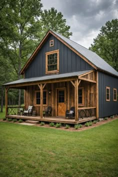 a small house with a porch and covered in wood, surrounded by green grass and trees