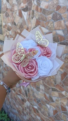 a person holding a bouquet of flowers with butterflies on it's wings, in front of a stone wall