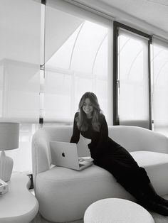 a woman sitting on a white couch with a laptop in her lap and looking at the camera