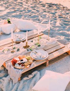 a table set up on the beach with plates and silverware