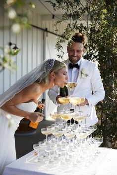 a bride and groom standing next to a table filled with glasses of wine, champagne