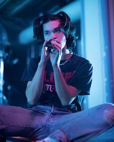 a young man sitting on the floor with his hands in his mouth while holding a cell phone