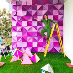 a man standing on a ladder in front of a wall made out of pink cubes