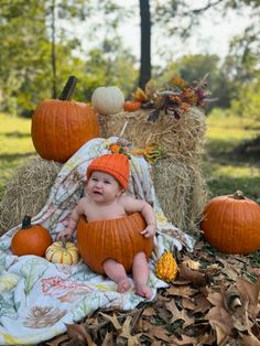 a baby sitting on top of a pile of hay next to pumpkins