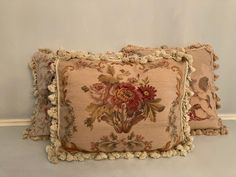 two decorative pillows with tassels on top of each pillow, one in red and the other in beige