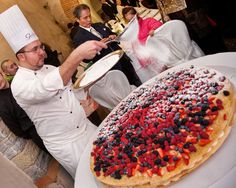 a man in chef's hat holding a plate with food on it and people standing around