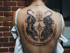 the back of a woman's neck with two tiger tattoos on it