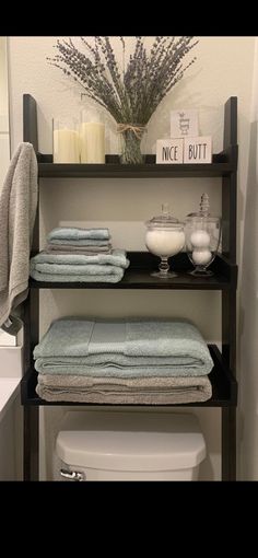 a shelf with towels, candles and other items on it next to a toilet in a bathroom