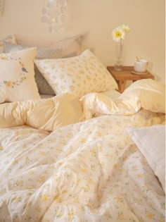 an unmade bed with white sheets and yellow flowers on the pillowcases in front of it