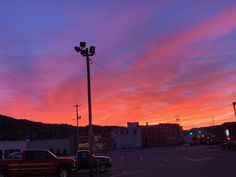 a red truck parked in a parking lot next to a street light and buildings at sunset