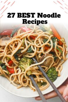 two hands holding chopsticks over a plate of noodles with broccoli and mushrooms